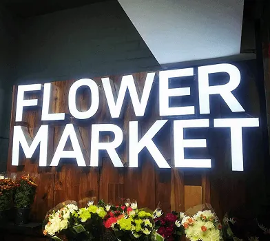 Illuminated 'Flower Market' wall sign above a floral display.
