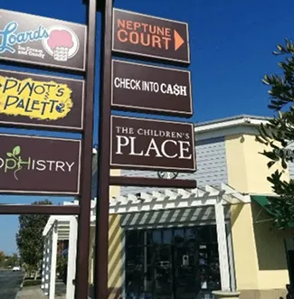 Multi-tenant pylon sign listing plaza stores beside a shopping center.