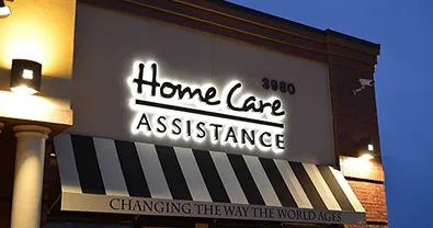Illuminated 'Home Care Assistance' storefront sign at night.