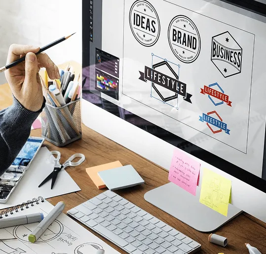 Designer workspace with logo concepts on a computer screen and sketch tools on the desk.